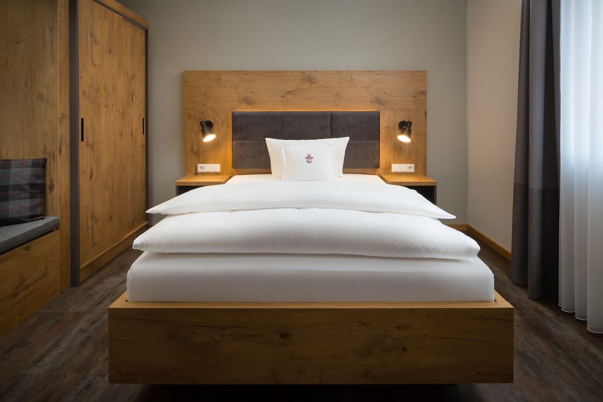Una cama bien tendida con un cabecero de madera, dos lámparas de noche y una mesita de noche de madera.