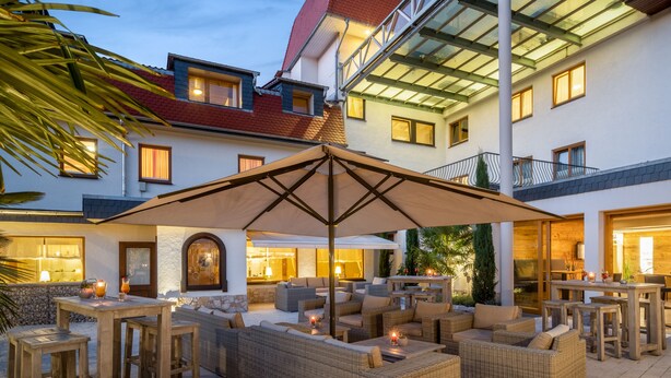 Un patio al aire libre con mobiliario de mimbre, una sombrilla grande y una zona de bar con iluminación.