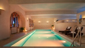 Una piscina interior con suelo de baldosas, una zona de estar hundida con sillones reclinables y una pequeña escalera que conduce a la piscina.