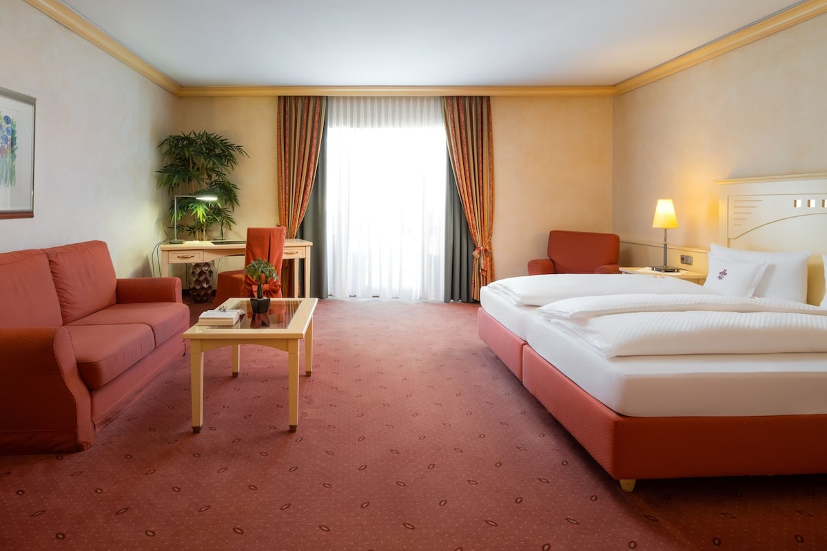 Habitación de hotel con cama, sofá, escritorio, silla, lámpara y planta.