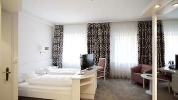 A hotel room with a bed, a desk with a TV, a chair, and a small table.