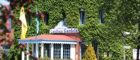 Un edificio llamado Landhaus Gardsels con techo rojo y columnas blancas.