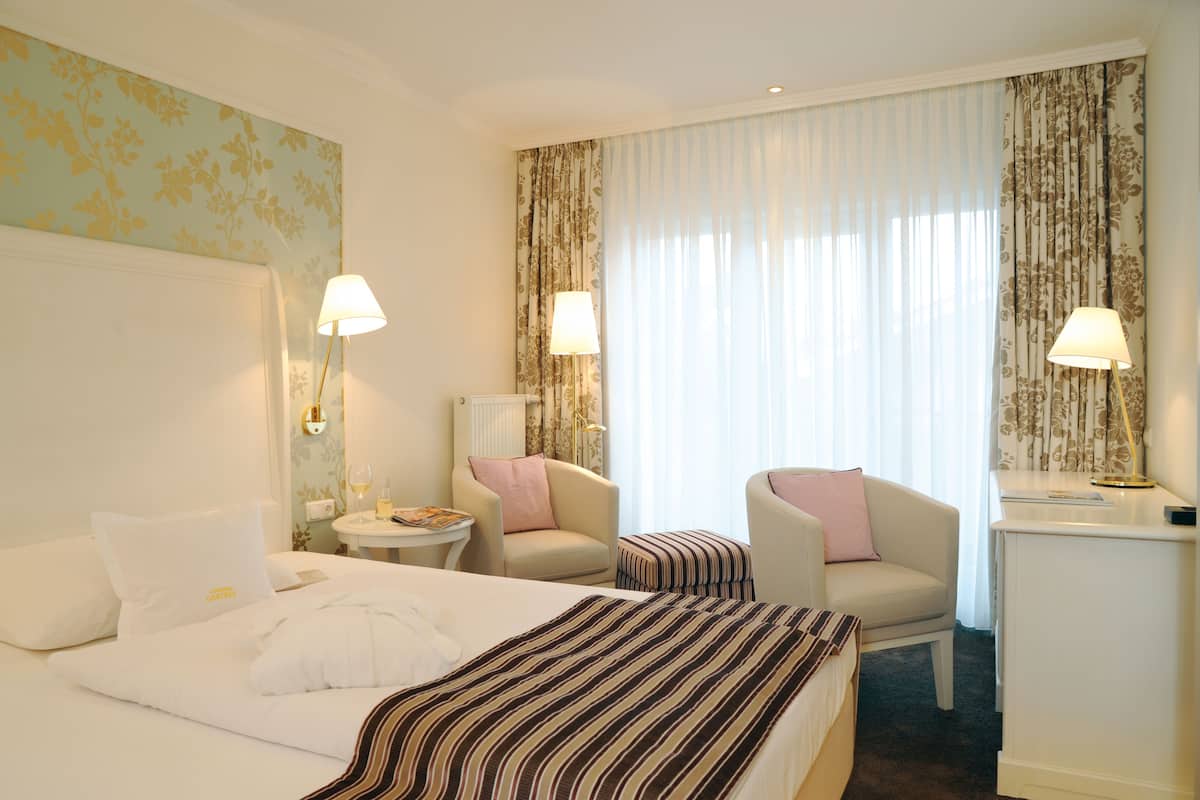 Ein Hotelzimmer mit zwei Betten, einer Sitzecke mit Stuhl und Tisch sowie einem Schreibtisch mit Lampe.