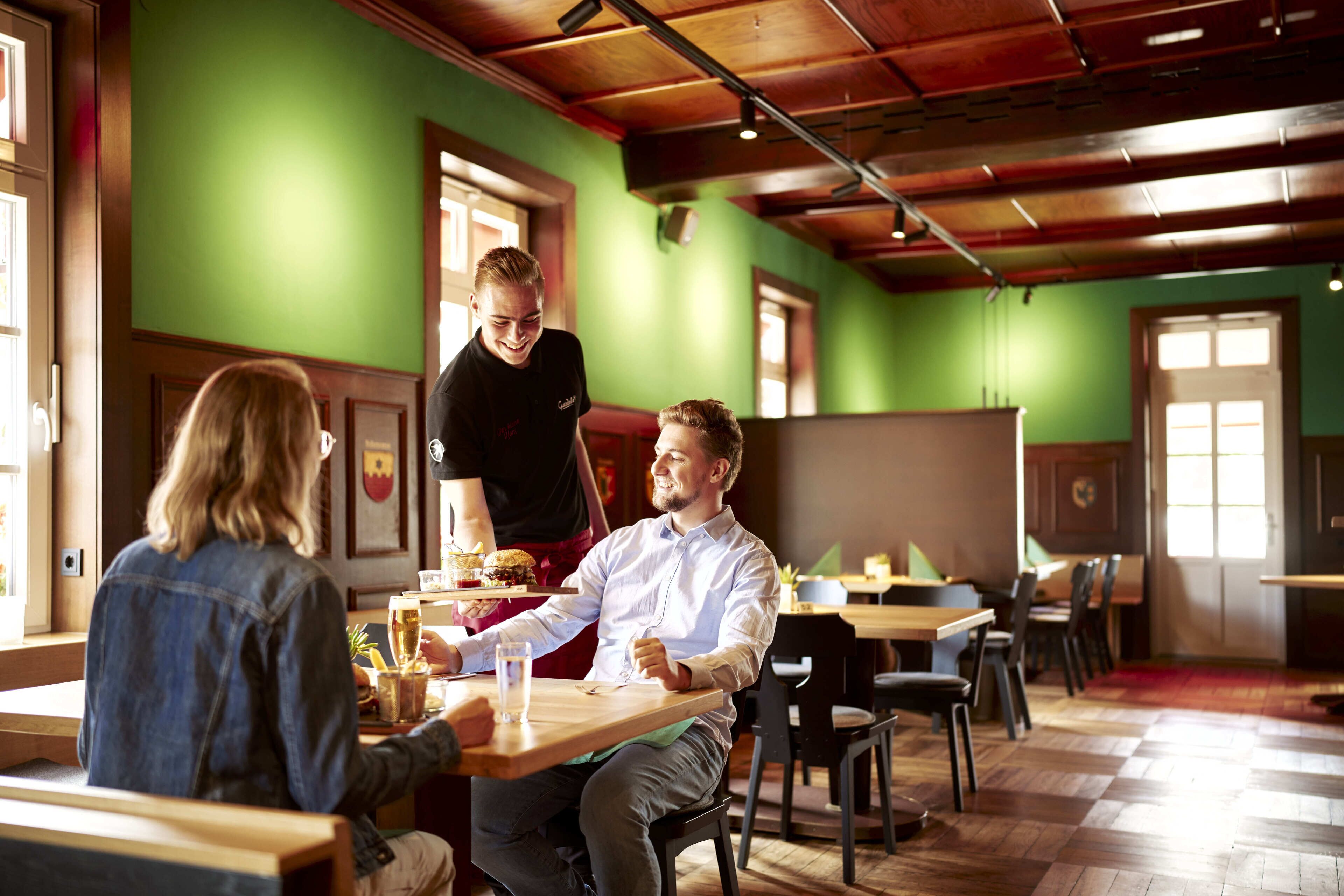 A restaurant with wooden tables and chairs, a green wall, and a wooden ceiling.