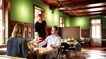 A restaurant with wooden tables and chairs, a green wall, and a wooden ceiling.