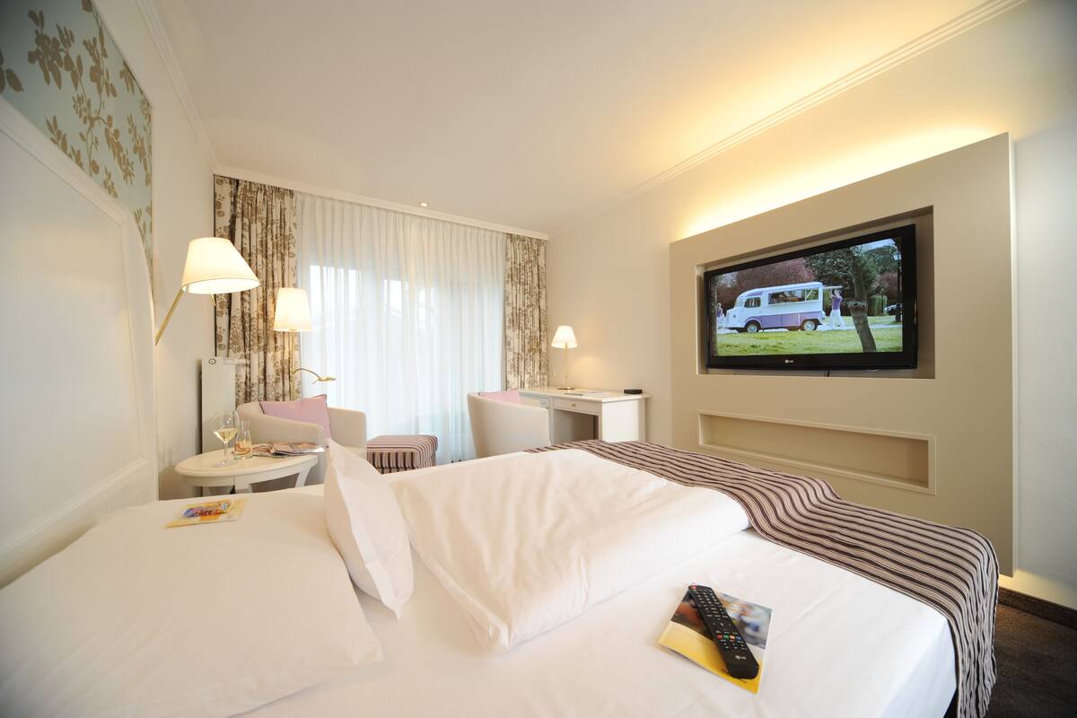 Ein Hotelzimmer mit einem Bett, einem Schreibtisch, einem Sessel, einem Fernseher und einem Fenster mit Vorhängen.