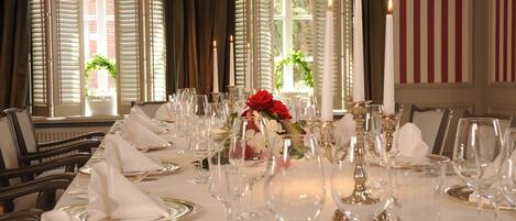 Un comedor formal con una larga mesa dispuesta para una comida, con manteles blancos, cubiertos y velas.