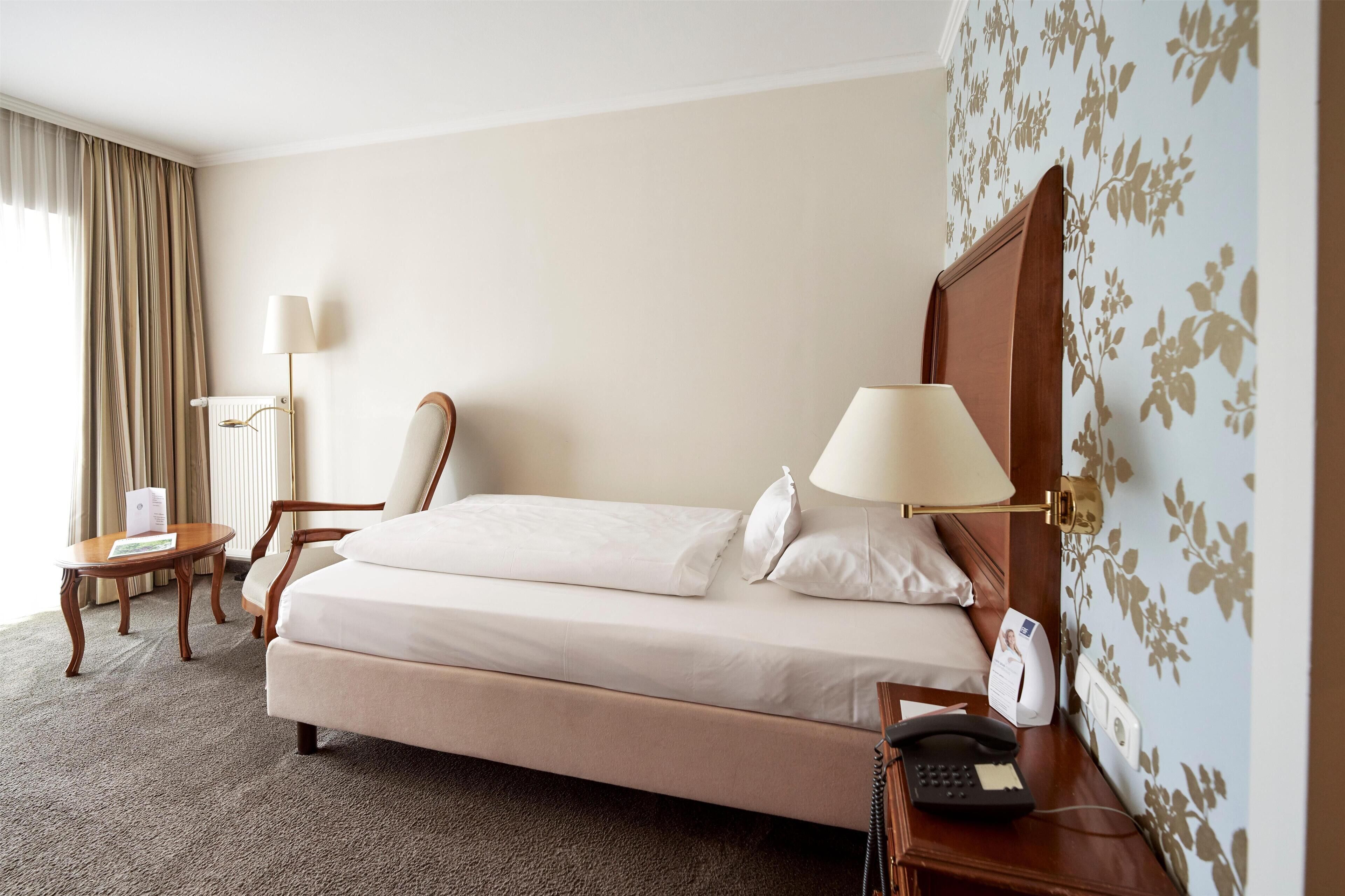 Ein Hotelzimmer mit einem Bett, zwei Nachttischlampen, einem Holznachttisch, einem Telefon und einem kleinen Tisch mit einer Lampe.