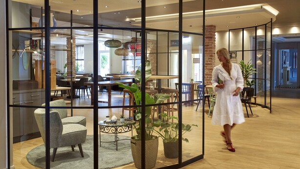 A modern interior with a glass partition, wooden flooring, and a dining area with chairs and tables. - Ringhotel Landhaus Gardels (Sankt Michaelisdonn)