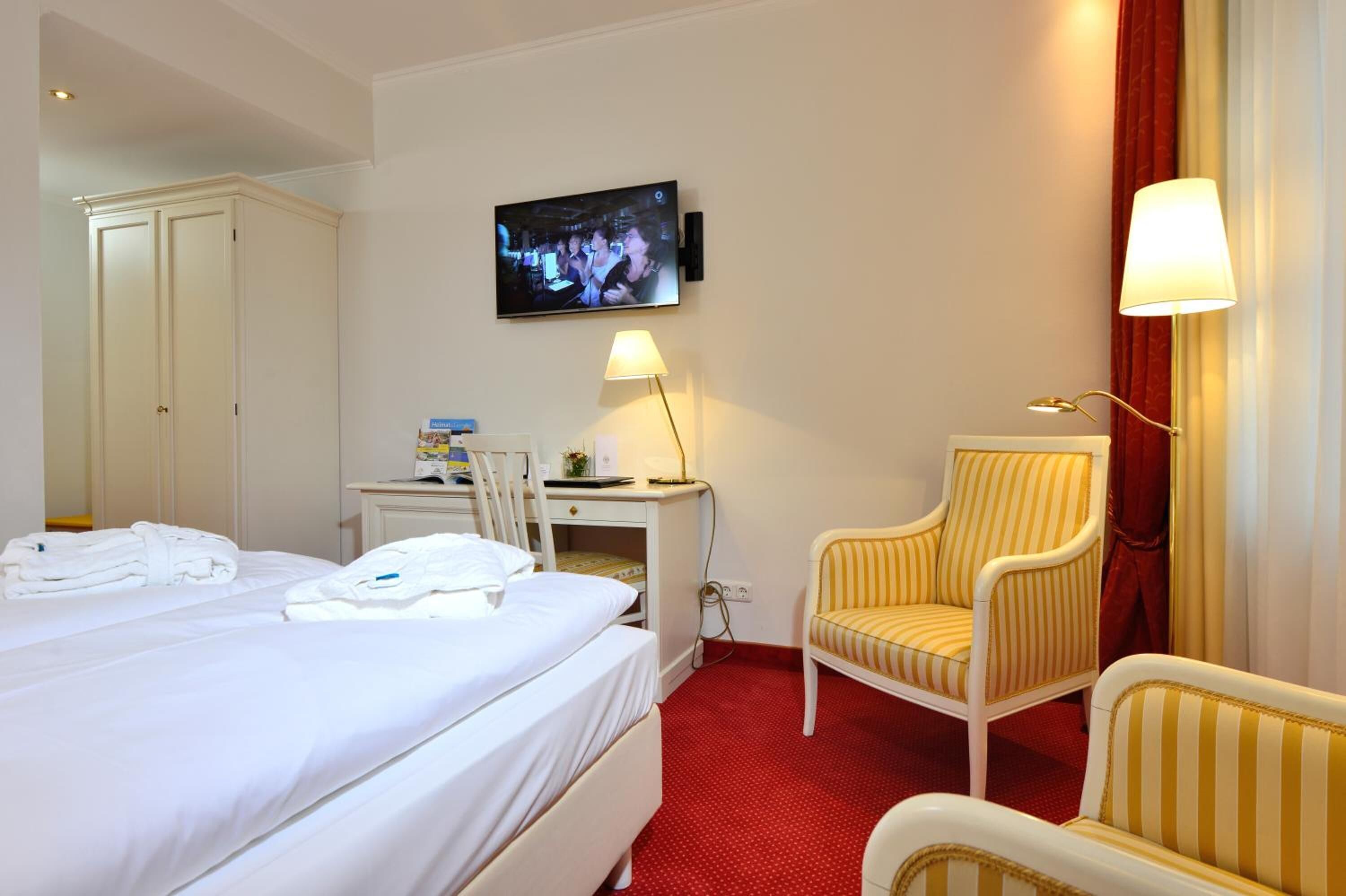 A hotel room with a bed, a desk with a chair, a television, and a lamp.