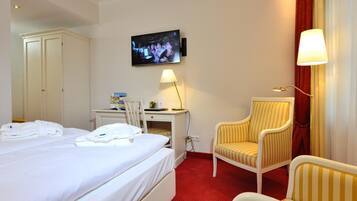 Una habitación de hotel con cama, escritorio, silla, televisor y lámpara.