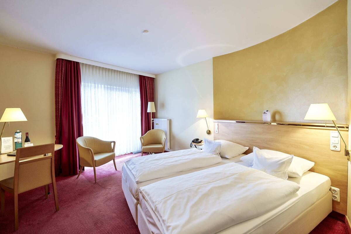 Ein Hotelzimmer mit zwei Betten, einem Schreibtisch, einem Stuhl und einer Lampe.