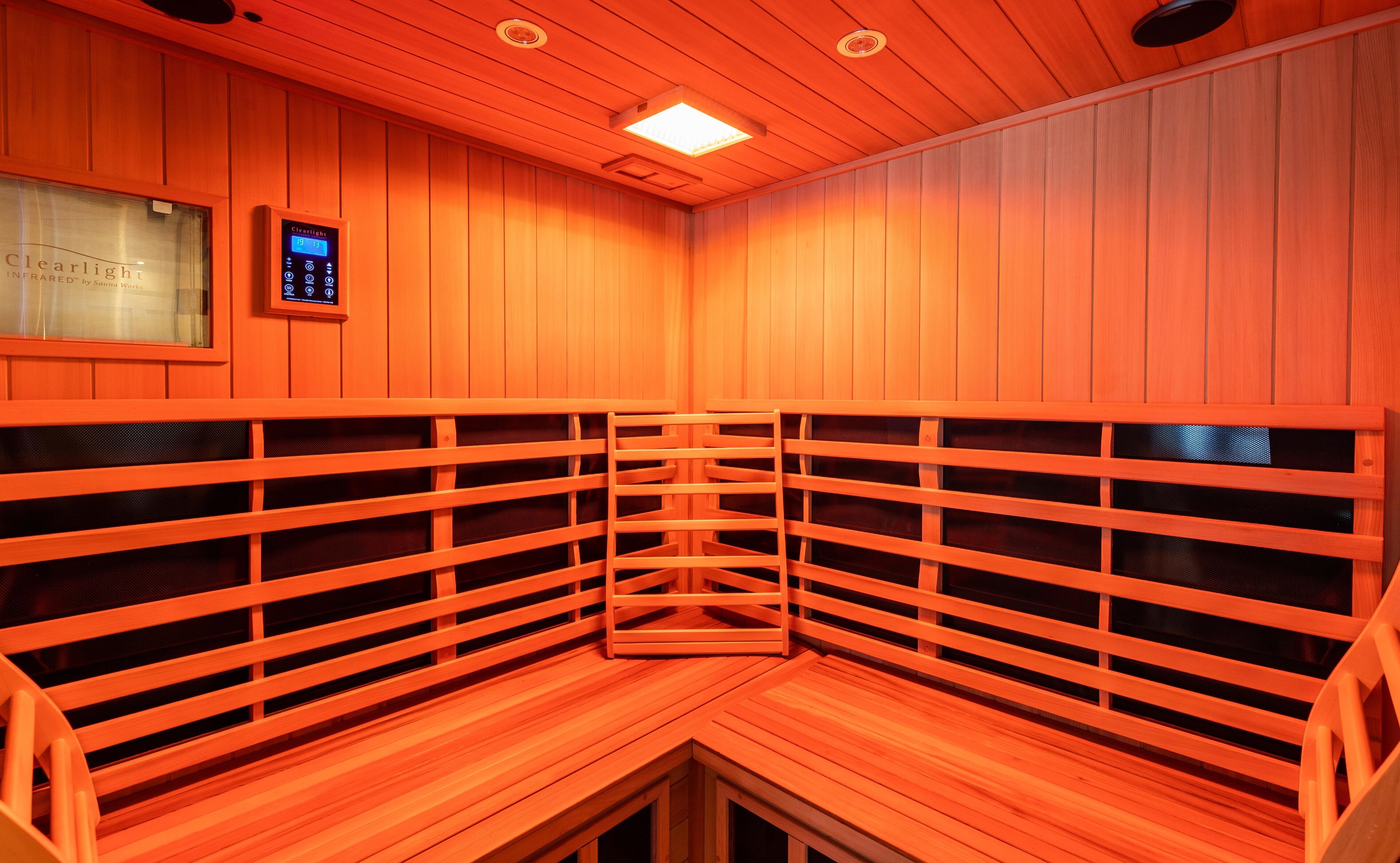 Een sauna met houten banken in een halve cirkelopstelling, een bedieningspaneel en een plafondlamp.