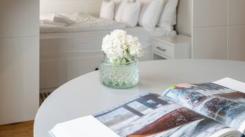 Ein modernes Schlafzimmer mit einem weißen Bett, einem Nachttisch und einer Vase mit weißen Blumen.