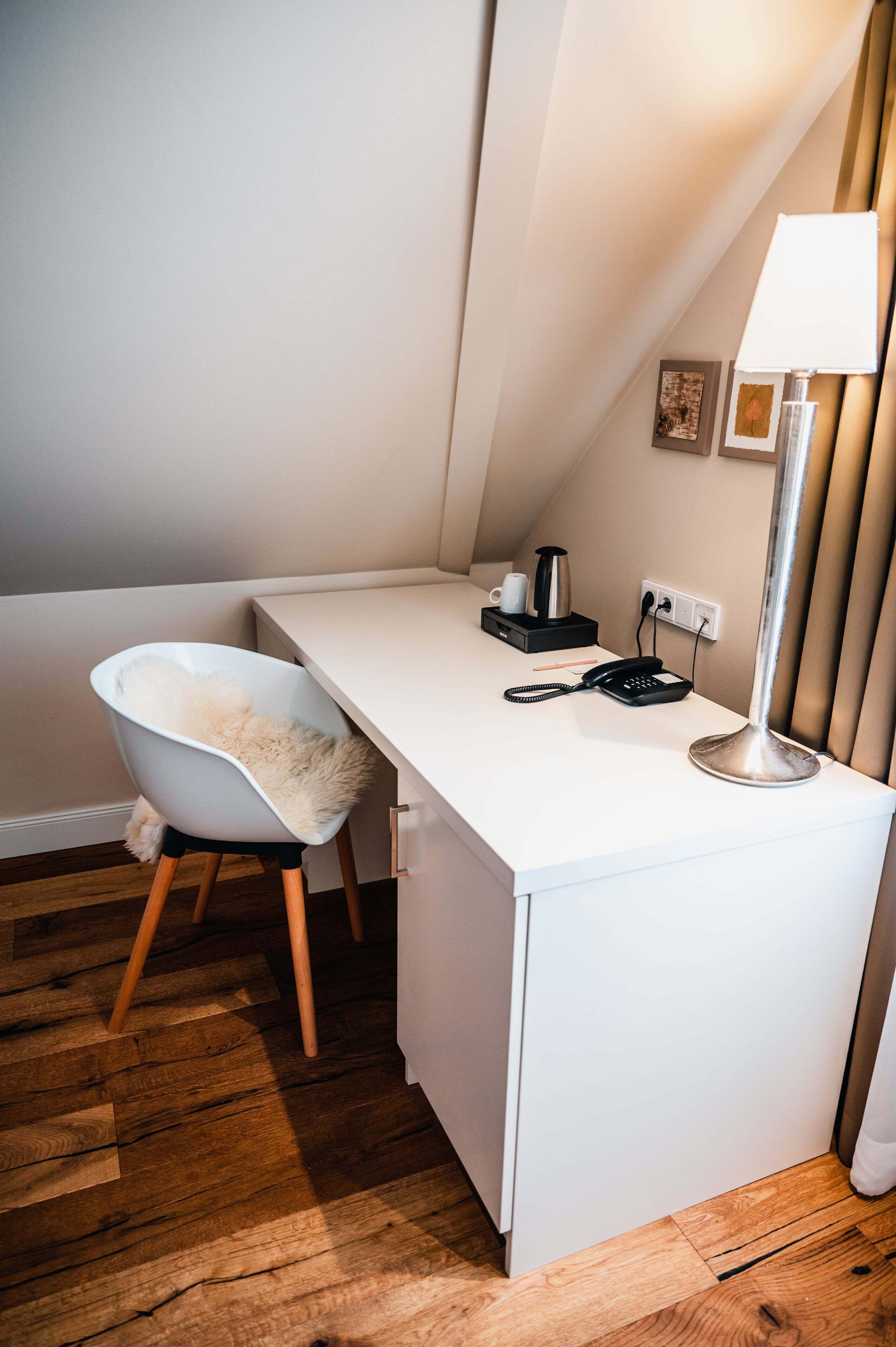 A small, white desk with a chair, a lamp, and a telephone.