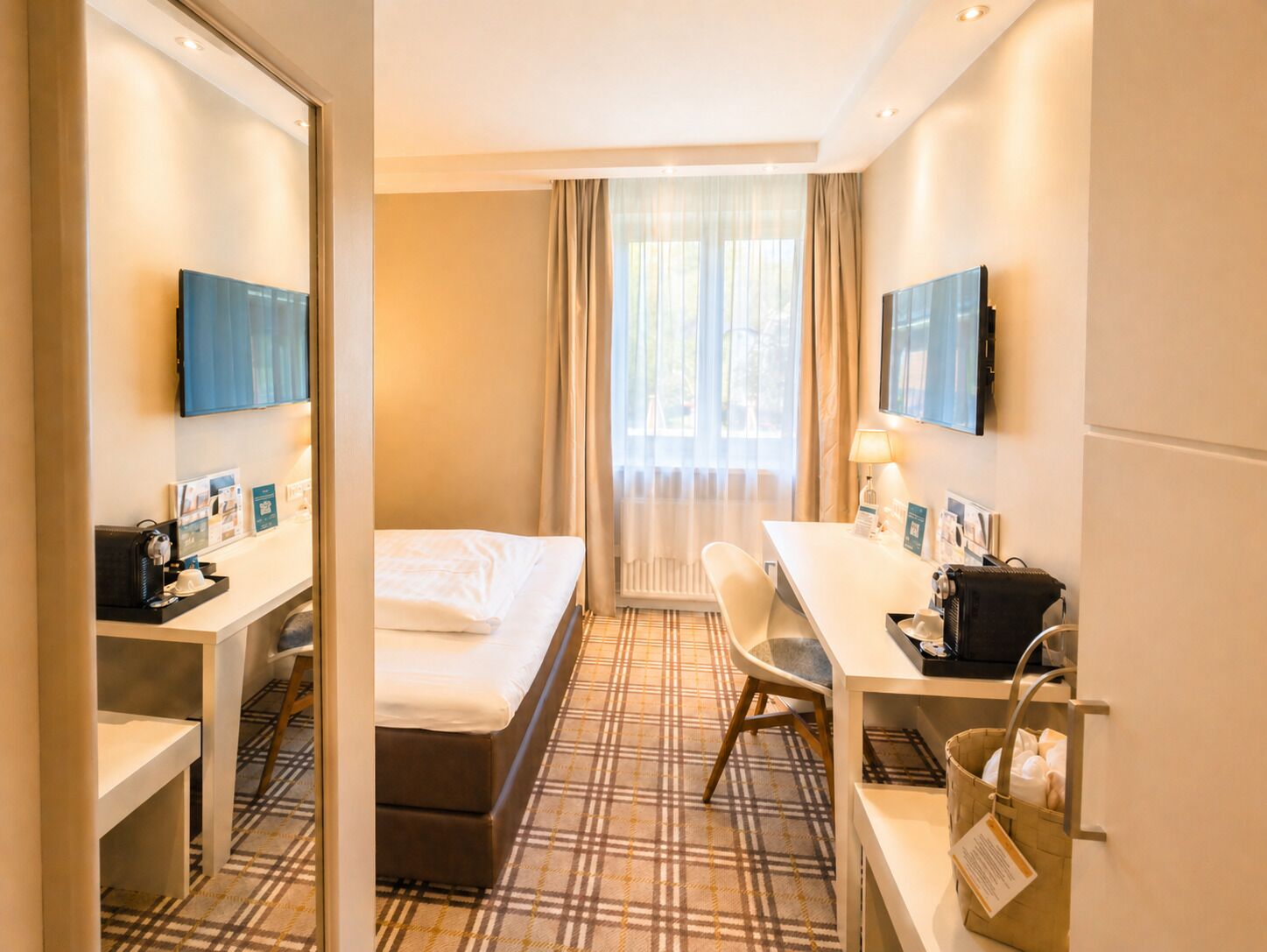 A hotel room with a bed, a desk, a chair, a TV, and a window with curtains.