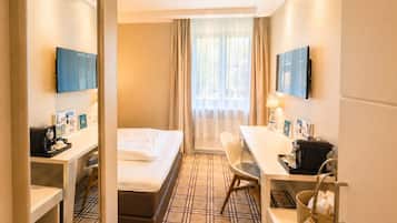 A hotel room with a bed, a desk, a chair, a TV, and a window with curtains.