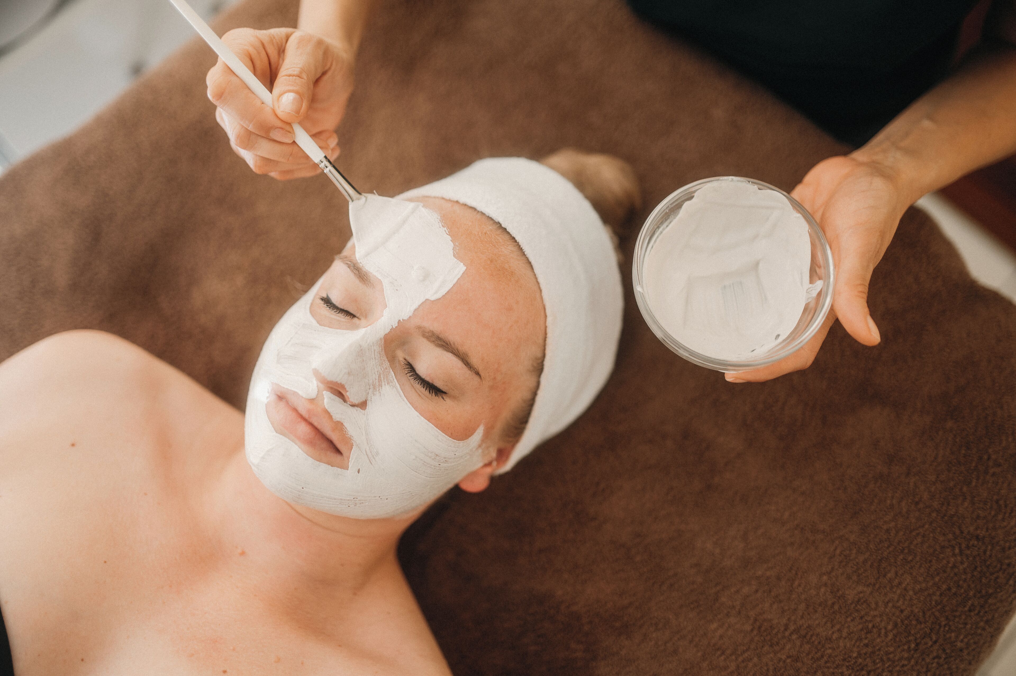 A person lying on a brown towel receiving a facial treatment.