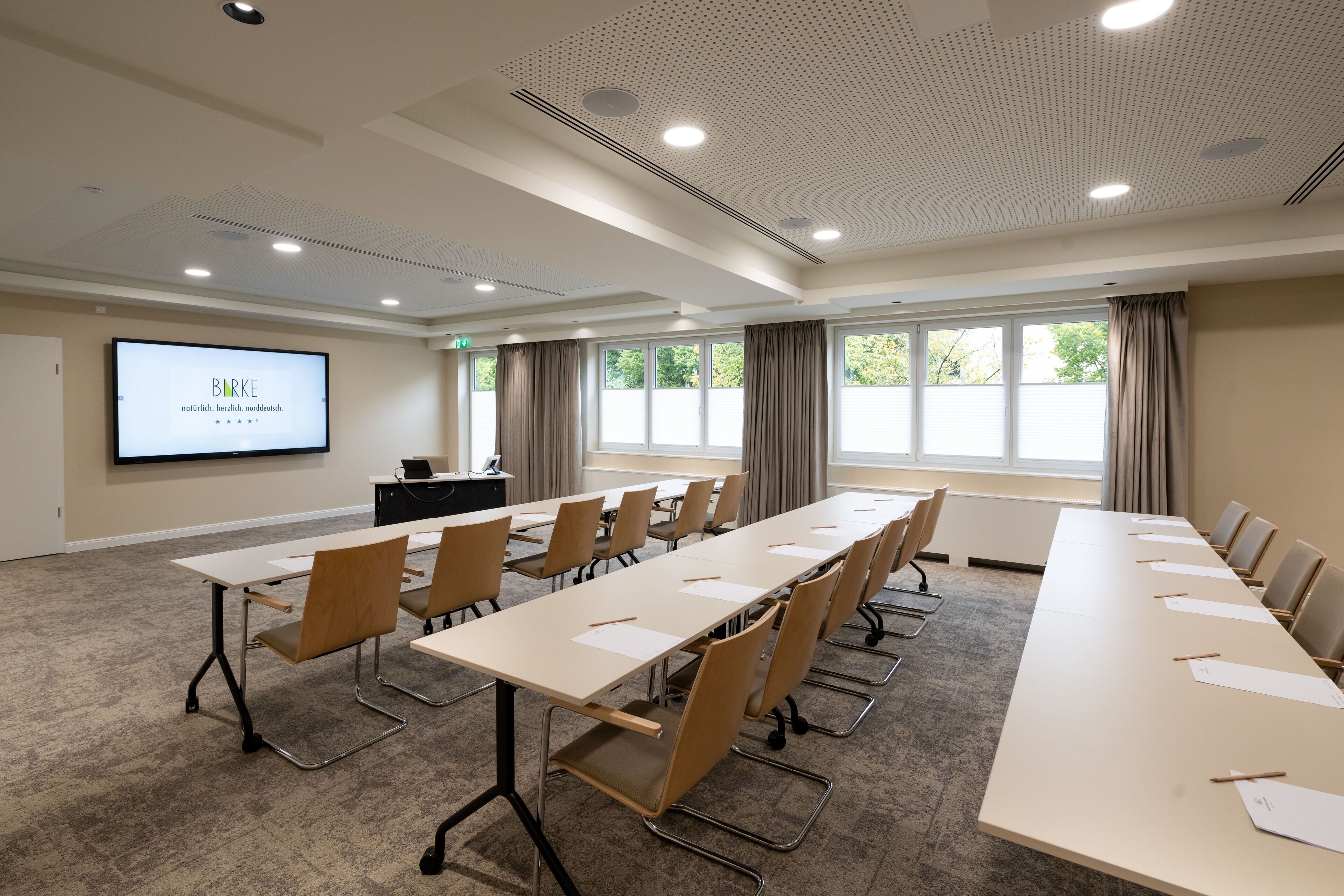 A conference room with a long table, chairs, a projector screen, and large windows.