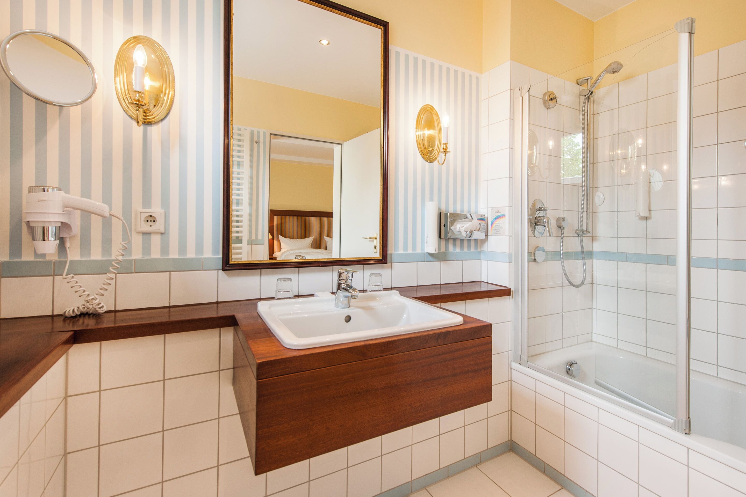 Un baño con tocador de madera, un espejo grande, ducha y secador de pelo.