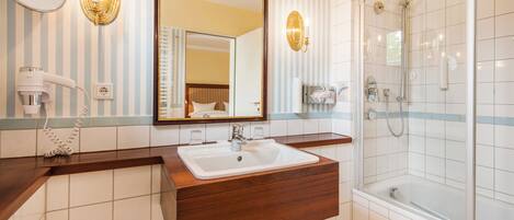 Un baño con tocador de madera, un espejo grande, ducha y secador de pelo.