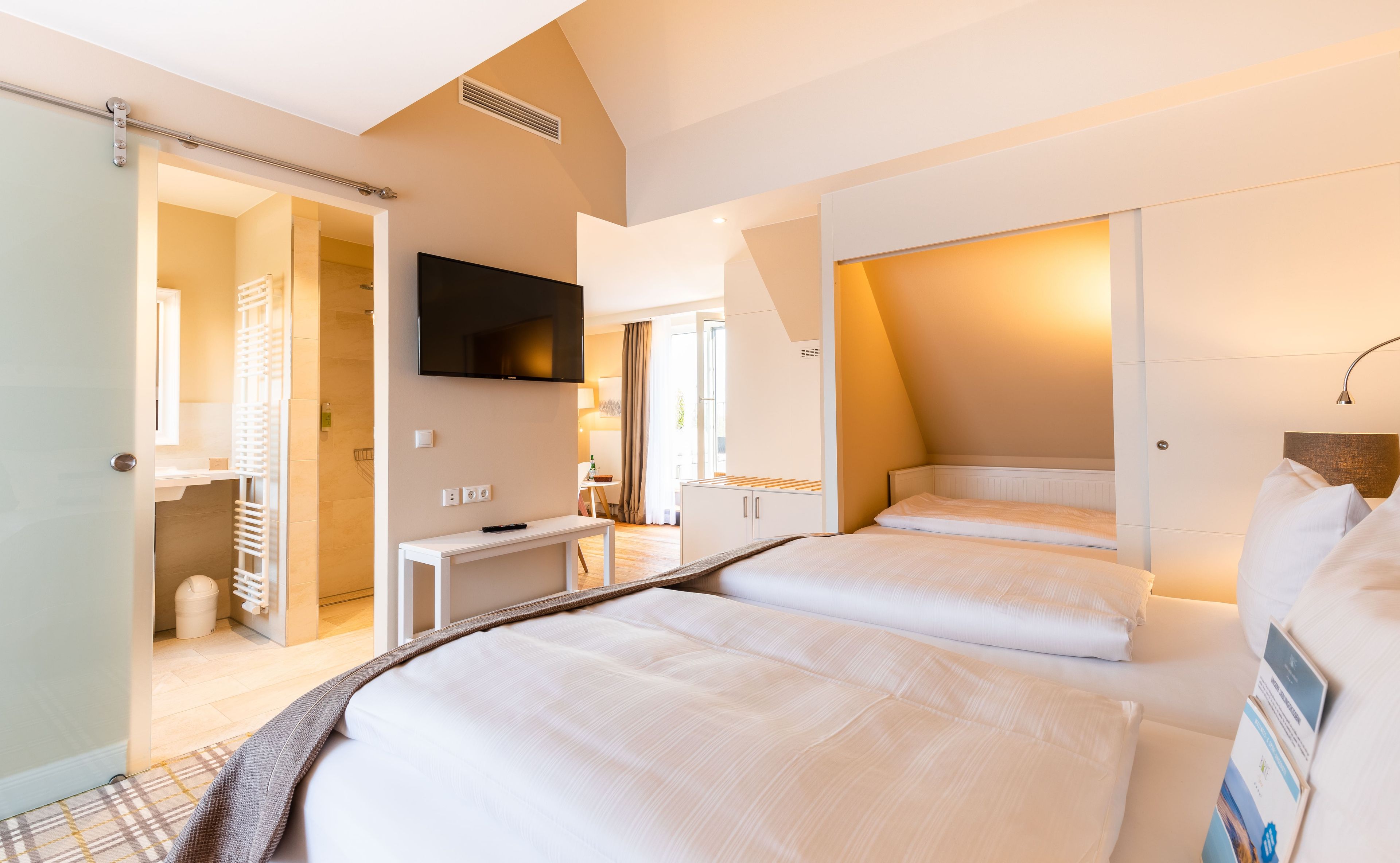 A hotel room with two beds, a TV mounted on the wall, and a desk with a chair.