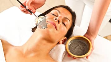A person receiving a facial treatment with a brush and a bowl of product.