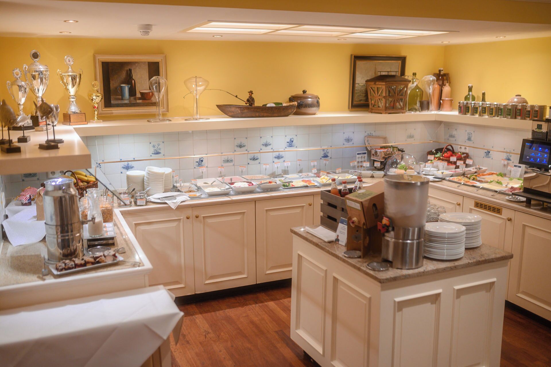Montaje de bufé con diversos alimentos y aderezos, una máquina de café y objetos decorativos en estanterías.