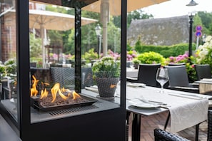 Un área de comedor al aire libre con una parrilla, plantas en macetas y asientos exteriores.