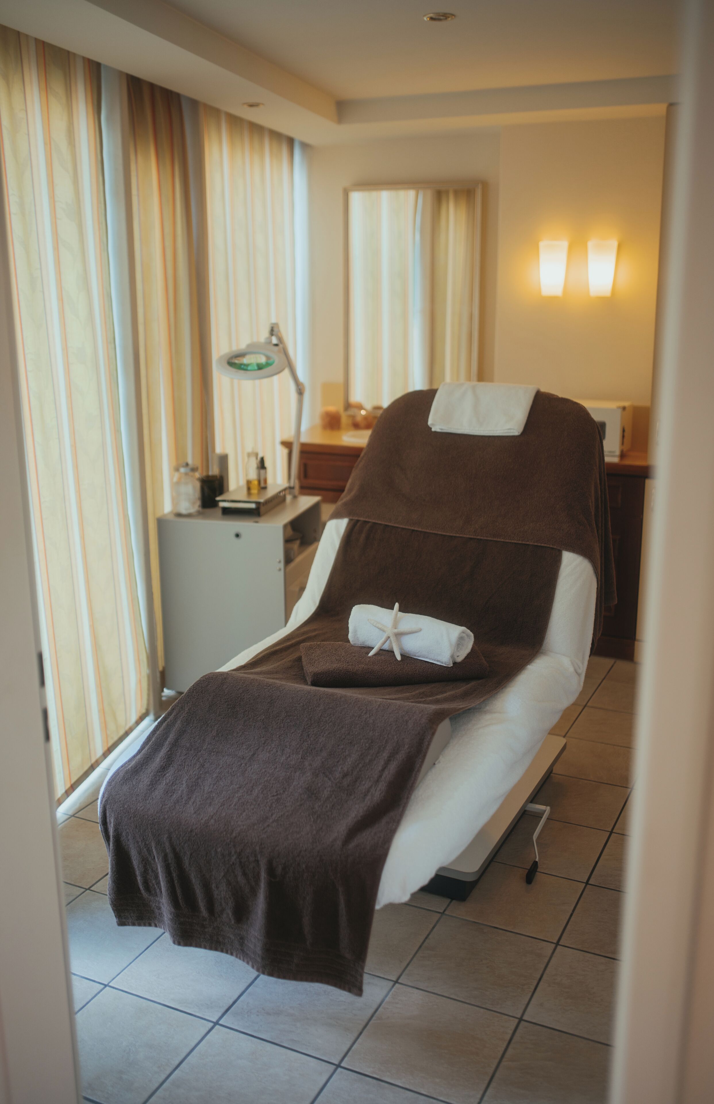 Una habitación de hotel con cama, mesita de noche, lámpara, espejo y cortinas.