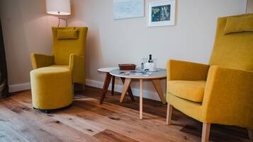 Een kamer met twee gele fauteuils, een klein rond tafeltje met een mand en glazen, en een lamp.