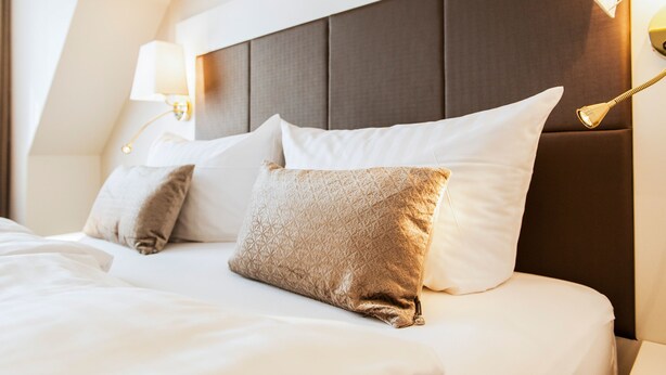 A neatly made bed with a headboard, two bedside lamps, and two pillows. - Hotel Birke, Ringhotel Kiel (Kiel)