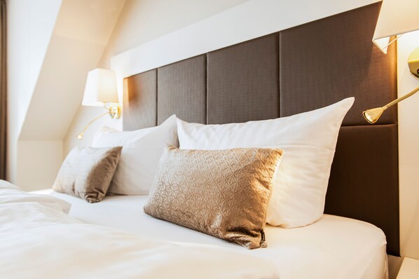 A neatly made bed with a headboard, two bedside lamps, and two pillows. - Hotel Birke, Ringhotel Kiel (Kiel)