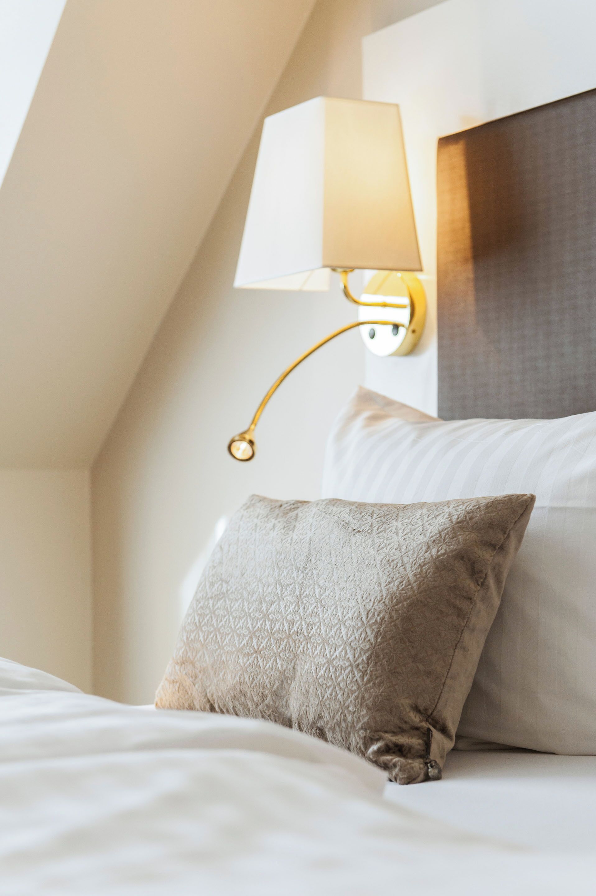 Ein ordentlich bezogenes Bett mit einer strukturierten Kopfstütze, einer Wandlampe und einem Kopfteil.