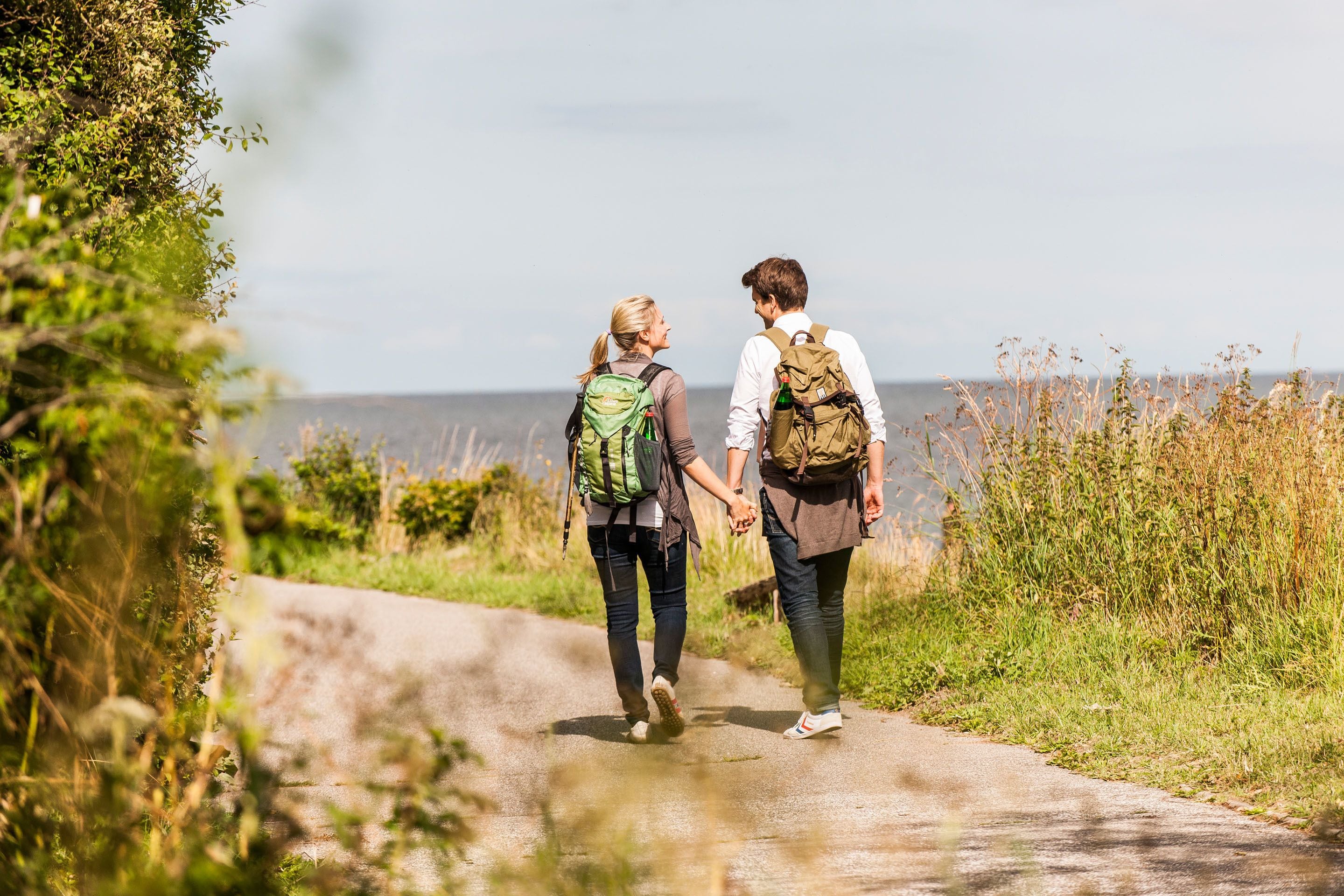 Two people walking on a narrow path surrounded by greenery.