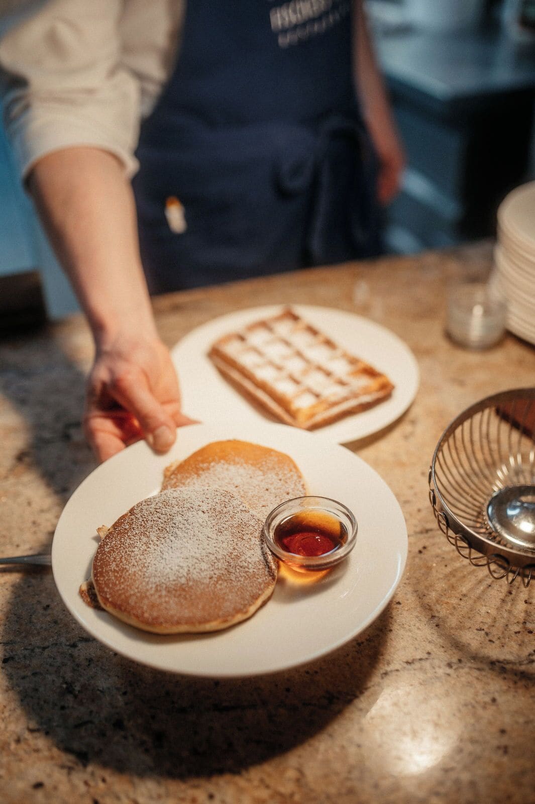 Une assiette avec des crêpes et du sirop, un gaufre et un petit bol de sirop, le tout posé sur un comptoir.