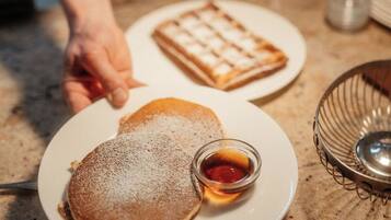Une assiette avec des crêpes et du sirop, un gaufre et un petit bol de sirop, le tout posé sur un comptoir.