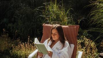 Une personne est allongée sur une chaise, appuyée sur un coussin à carreaux, et lit un livre.