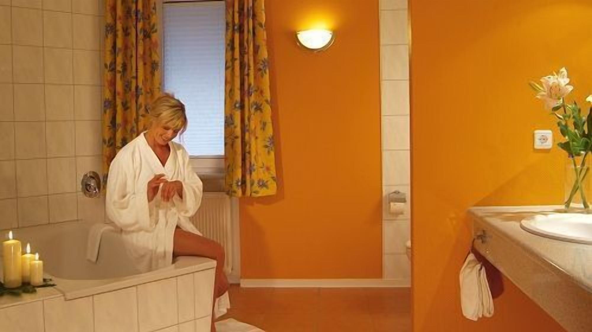 A bathroom with a bathtub, a sink, and a mirror. There are candles on the side of the bathtub.