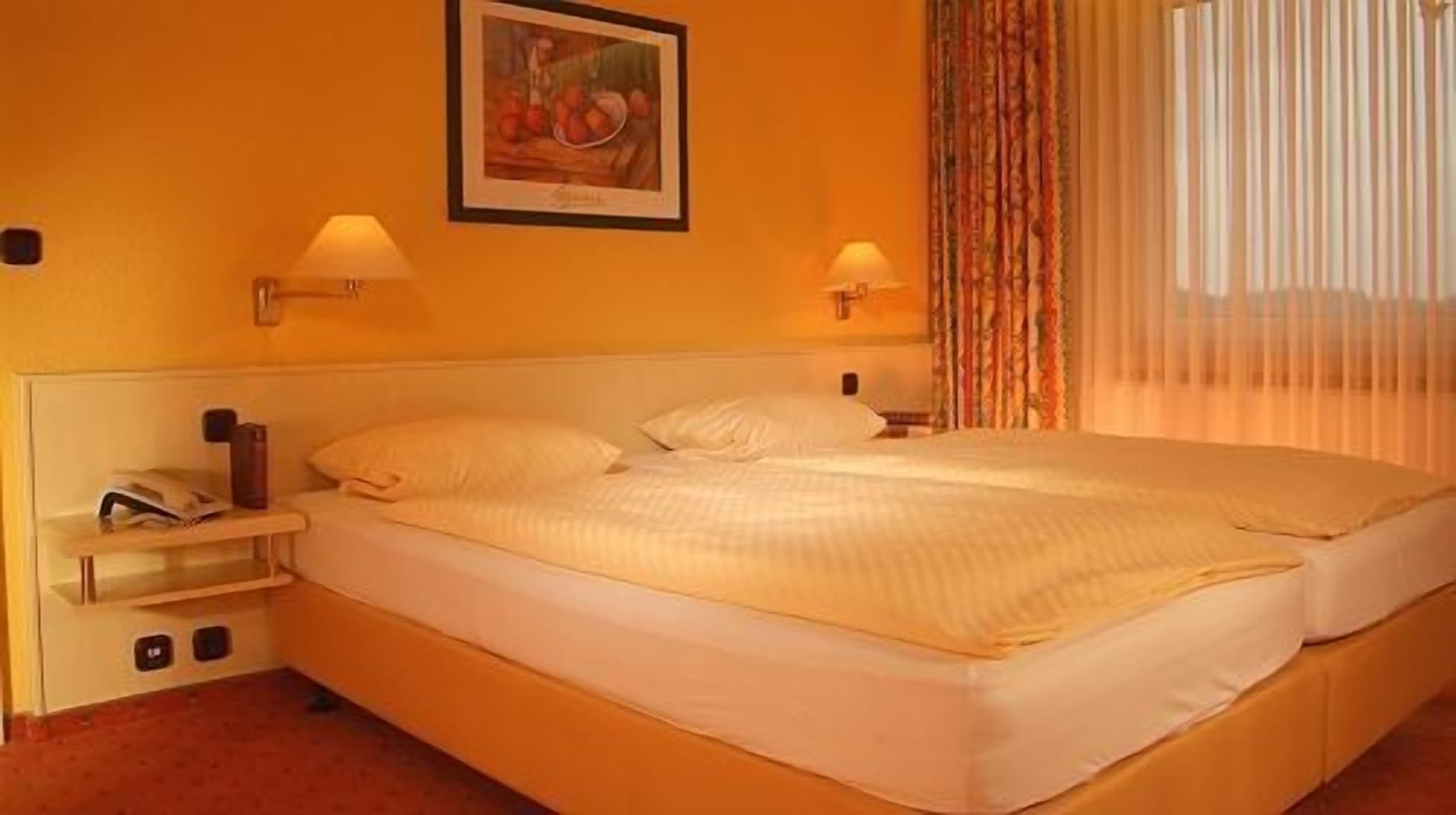 Ein Hotelzimmer mit einem großen Bett, zwei Nachttischlampen, einem Nachttisch mit Telefon und einem Bild an der Wand.