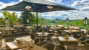 An outdoor patio with wicker furniture, tables, and chairs, featuring a view of the landscape. - Ringhotel Roggenland (Waldeck)