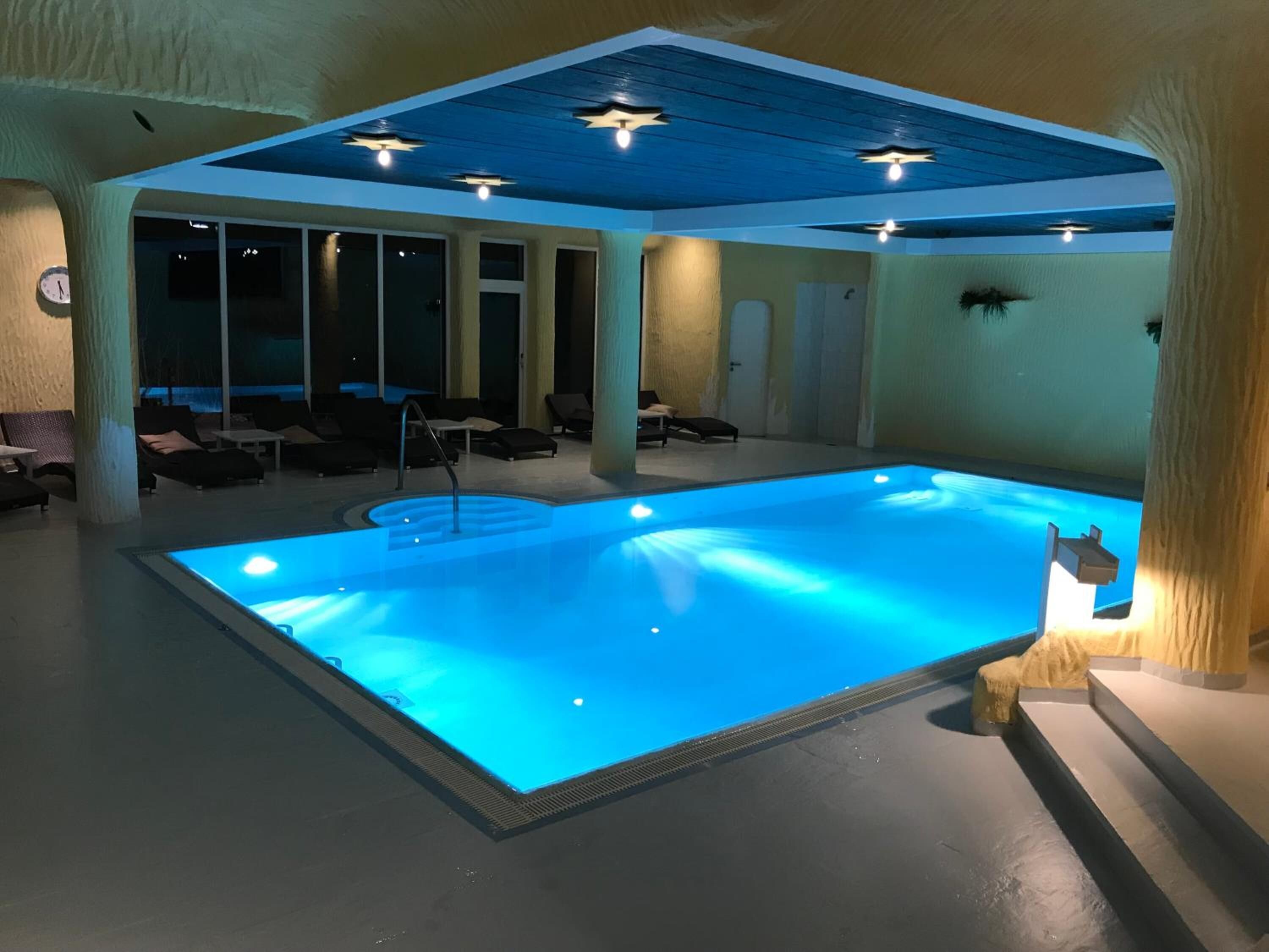 An indoor swimming pool with a blue-lit water feature, lounge chairs, and a ceiling with star-shaped lights.