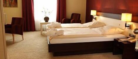 Una habitación de hotel con una cama grande, dos mesitas de noche, una silla y un ventanal con cortinas.