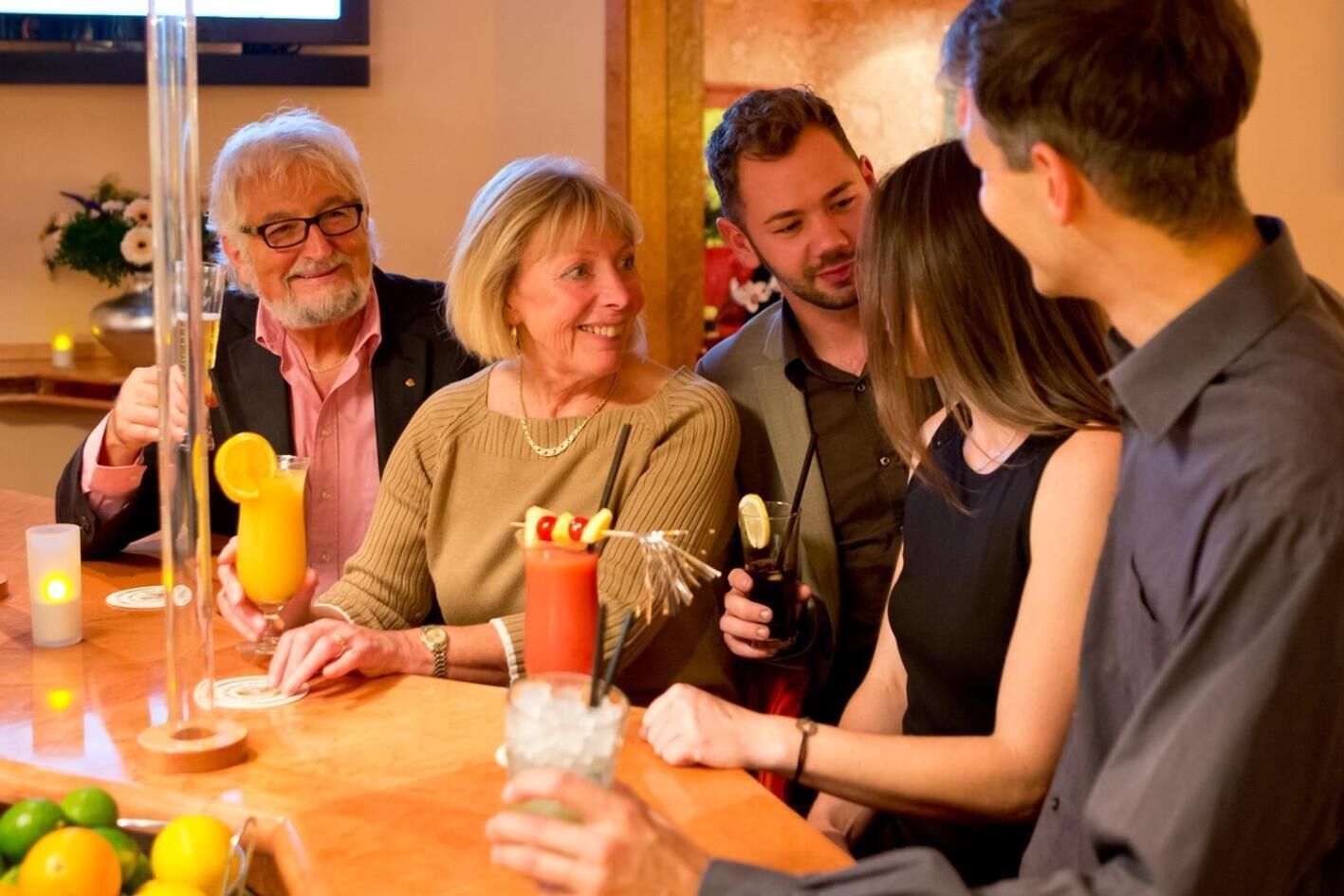 Eine Gruppe von Personen sitzt an der Bar, umgeben von Getränken und einer Obstschale.