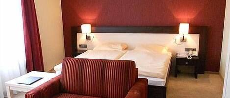 Een hotelkamer met een bed, twee nachtkastjes, een stoel en een klein tafeltje met een boek.