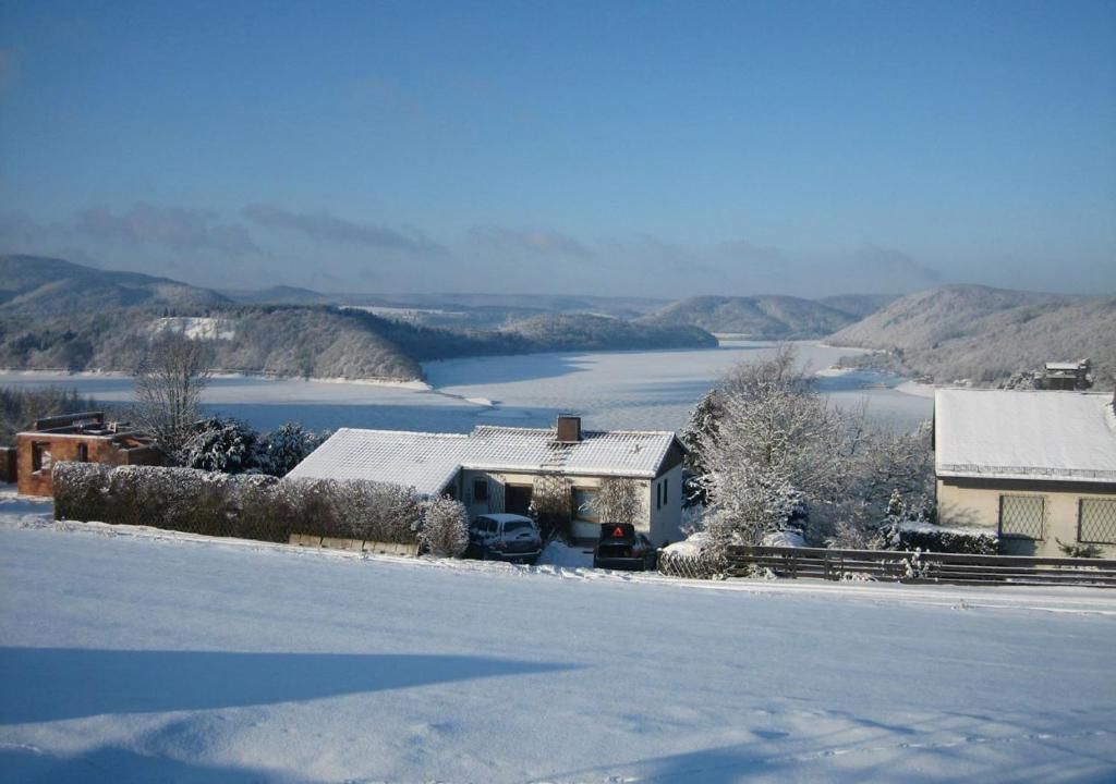 A rural landscape with snow-covered fields, a house with a garage, and distant hills.