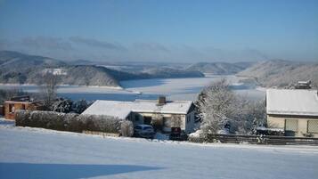 A rural landscape with snow-covered fields, a house with a garage, and distant hills.