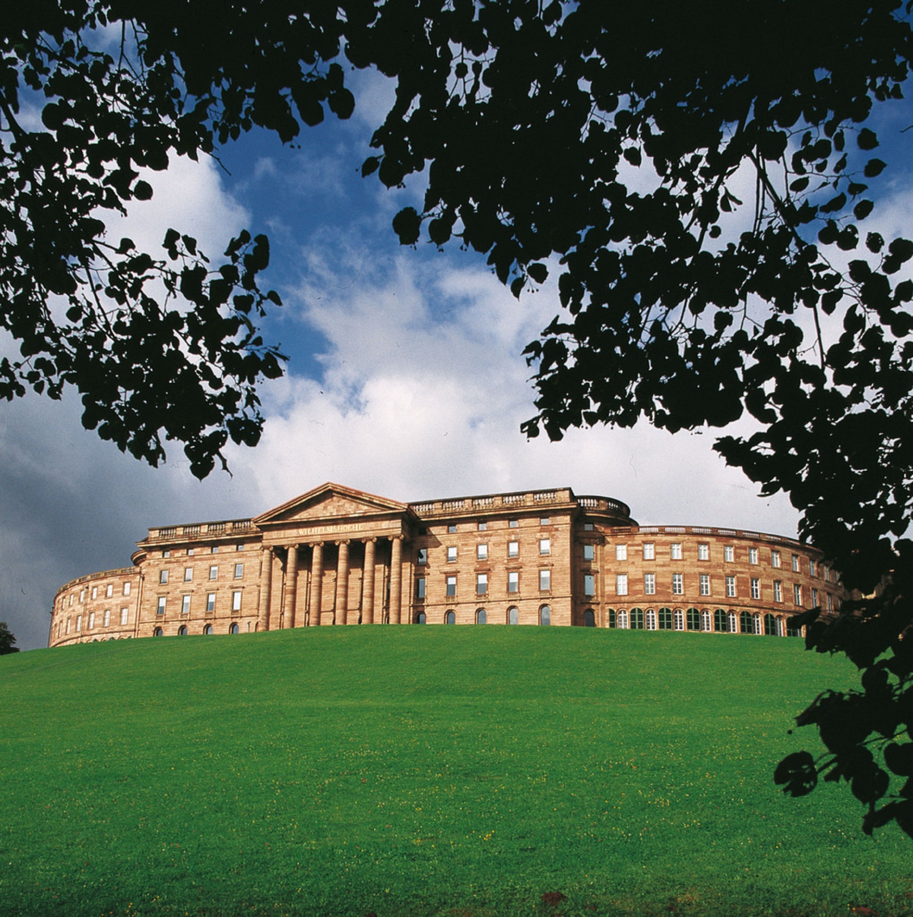 A large, classical building with a central entrance flanked by columns, surrounded by a well-maintained lawn.