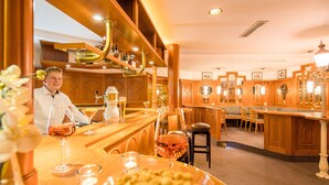 A bar area with wooden furniture, a counter, and a seating area with chairs and a table. - Waldhotel Schäferberg (Espenau)