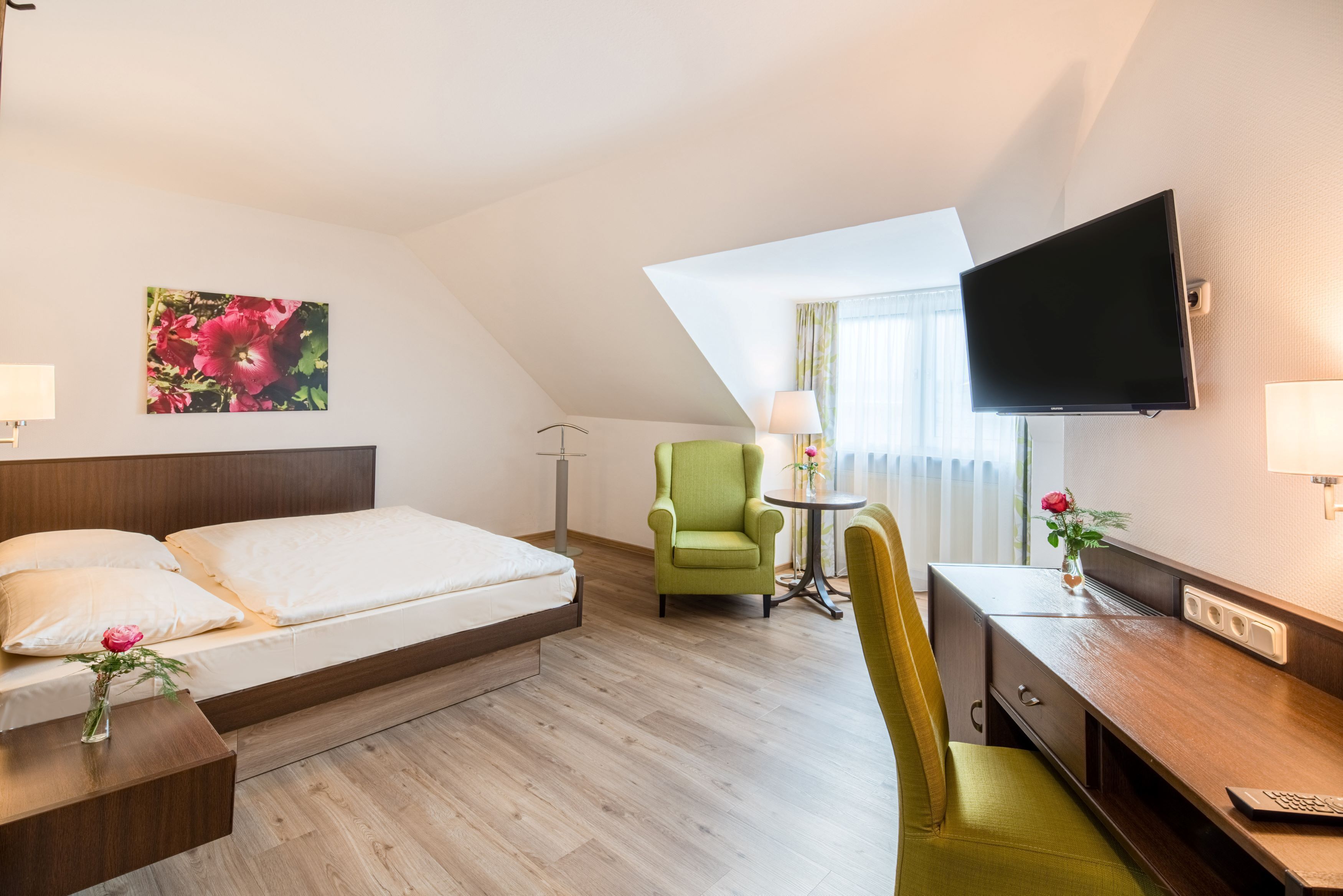 Camera d'albergo con un letto, una scrivania, una sedia, una televisione e una finestra con tende.